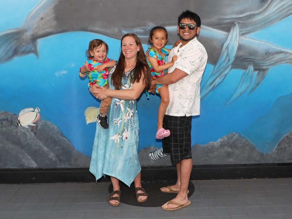Ms. Reynolds and her husband hold their two young children in front of a blue mural with painted whales.