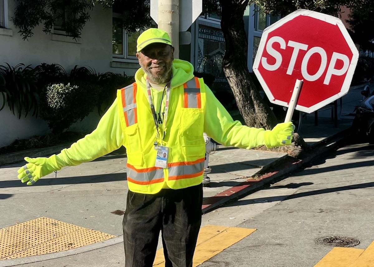 Mr. Fundi stands at a crosswalk intersection with a stop sign.